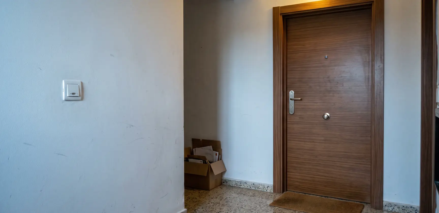 Puerta blindada de un piso vista desde el rellano, con el bombín y la manilla. Foto generada con IA.